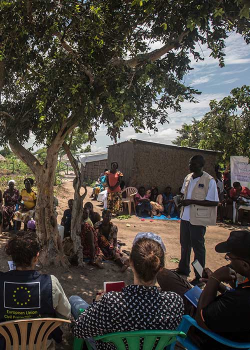 Journalists and others listening to local liaison officer working with Relief Hope Recovery (GOA), one of several partners of the European Commission’s Civil Protection and Humanitarian Aid department (ECHO) at Rhino refugee settlement, Uganda.